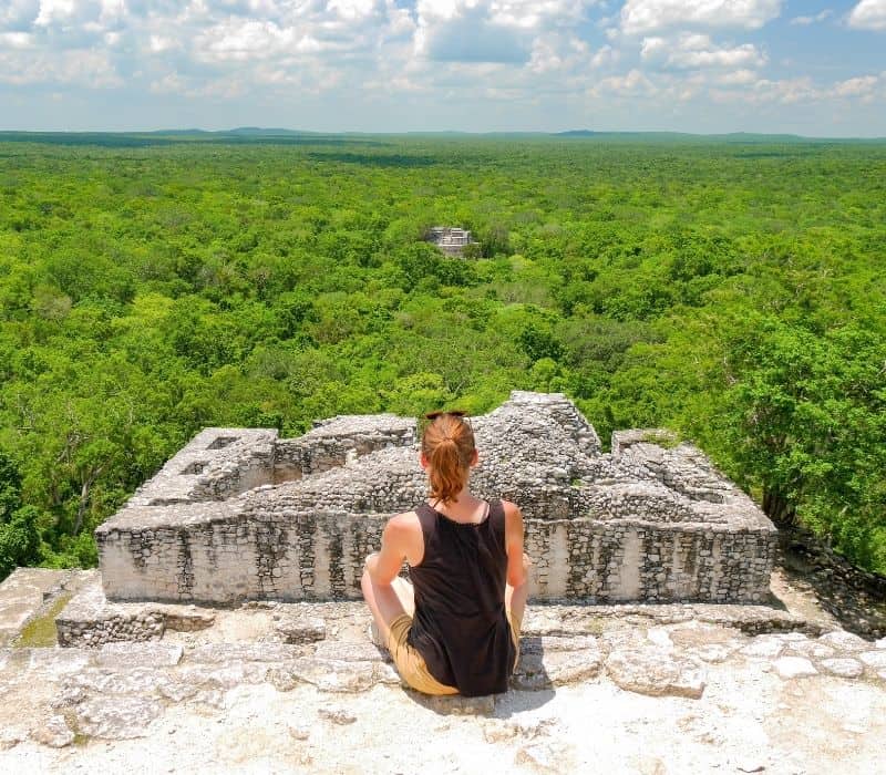 mujer en una camiseta sin mangas negra sentada en la cima de la pirámide maya en las selvas de méxico, ruinas de Calakmul, uno de los lugares más singulares para visitar en méxico