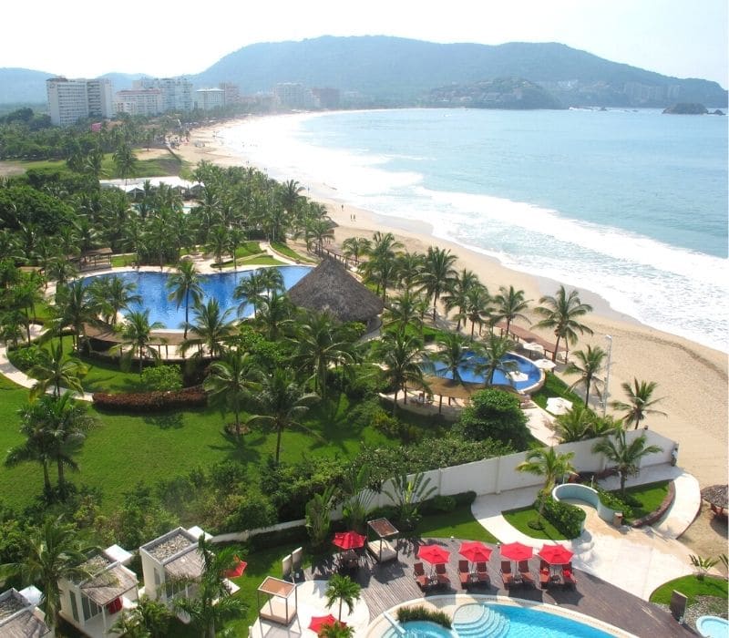 agradables resorts con piscinas y sillas de playa y un paisaje verde de palmeras en el océano pacífico con montañas al fondo en Ixtapa, una de las mejores ciudades mexicanas de playa