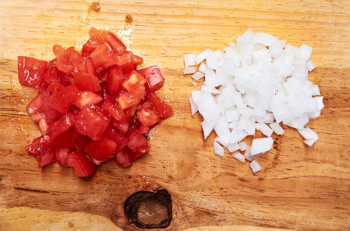 Tomates Roma picados y cebolla blanca sobre tabla de cortar de madera