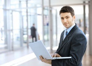 Joven empresario sonriente usando laptop en ubicación corporativa, interior.